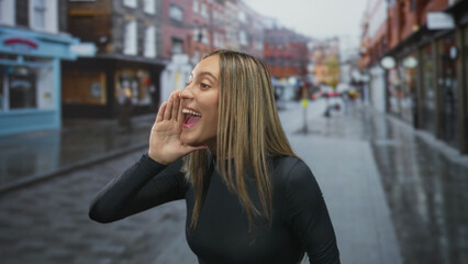 Fototapeta premium Woman cupping hand to mouth shouting on a wet urban street wearing black long sleeve top near storefronts; joy.