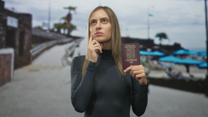 Young hispanic woman holding passport with finger to chin on street by seaside umbrellas, appearing to plan travel; thinking travel planning.