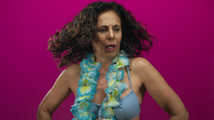 Hispanic middle-aged woman in a blue swimsuit and hawaiian lei stands against vibrant pink...
