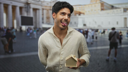 Man holding small wooden house model in one hand, other hand behind back, tongue out, standing...