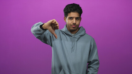 Man in gray hoodie shows thumbs down with visible thumb and neutral expression in studio; disapproval rejection.