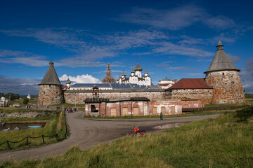 Historic stone fortress and monastery towers on Solovetsky Island, Russia, under a bright blue sky with visitors walking nearby.