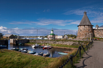 Historic harbor with boats and ancient stone monastery towers on Solovetsky Island, Russia, under a bright blue sky.