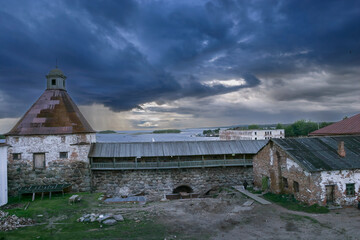 Dark storm clouds over historic stone walls and old buildings on Solovetsky Island in Russia, with dramatic light over the sea.