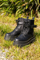 Black combat-style boots resting on rocky grass terrain