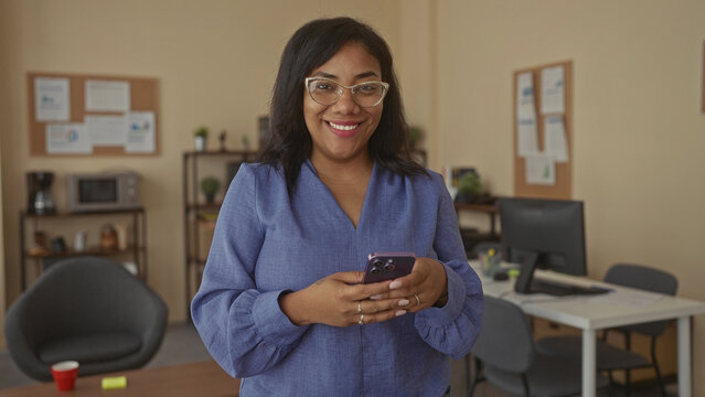 Woman holding smartphone with both hands and tapping screen with fingers at a desk in office building; connection.