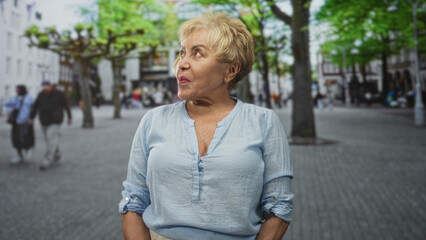 Senior hispanic woman in light blue blouse looks right with hands in pockets, slight smile and...