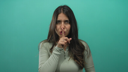Woman gesturing silence with finger on lips against a green isolated background, conveying a...