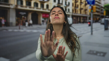 Fototapeta premium Woman gesturing stop on street with buildings in background, emphasizing urban hustle and outdoor life.