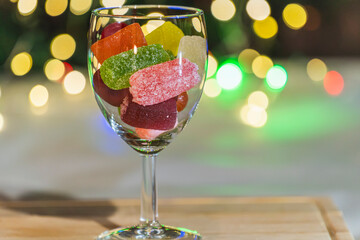 Glass filled with marmalade candies on wooden board with blurred bokeh