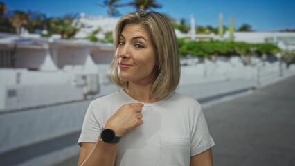 Woman smiles with eyes closed and points finger to chest in front of white building by palm tree; confidence self esteem pride.