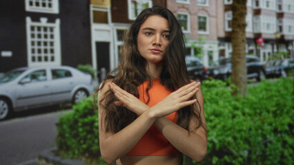 Young woman wearing bright orange crop top with crossed arms in front of chest on street; rejection.