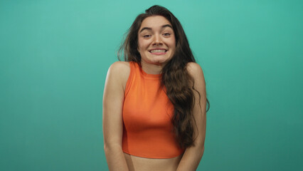 Woman with bare arms and midriff shrugs in a studio wearing an orange crop top and cringing tense shoulders; uncertainty.