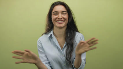 Woman wearing a striped shirt crossing her hands in x shape and laughing in front of a green wall in a studio; joy.