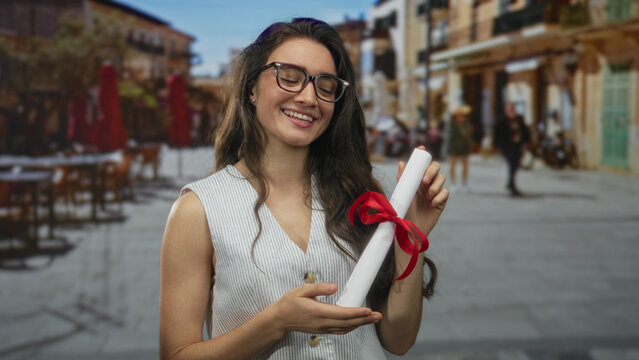 Woman holding rolled diploma tied with red ribbon pointing finger to document on busy city street; pride achievement.