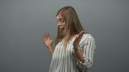 Woman tosses hair off face while glancing sideways in grey studio wearing striped blouse; surprise shock.