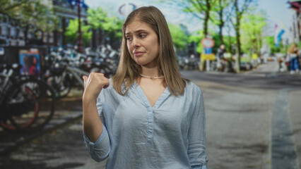 Fototapeta premium Blonde woman pointing thumb to street beside sunlit canal flanked by bicycles in amsterdam; skepticism.