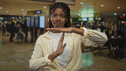 African american woman making a timeout hand gesture in an airport terminal near seating and...