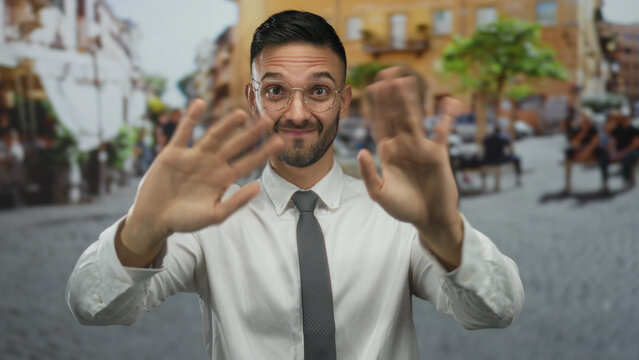 Young man in glasses and tie gestures playfully on a bustling urban street, embodying a vibrant city life.