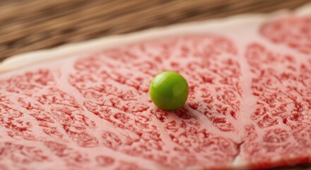 Close-up of raw marbled meat with a single, perfectly round green pea. The meat shows intricate textures and fat marbling, contrasted by the pea's smooth surface and vibrant color. Wooden backdrop