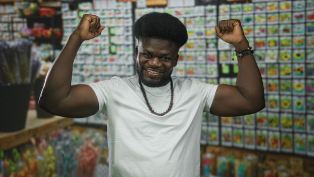 Man flexing biceps and smiling amid flower packets and seed displays in building flower market; confidence.