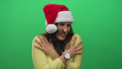 Woman wearing santa hat hugging bare arms in isolated green screen studio; coldness discomfort holiday.
