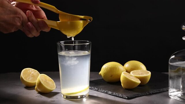Hands of Woman using citrus press to extract fresh lemon juice into glass beaker with water. Close-up shot in kitchen setting. High quality 4k footage