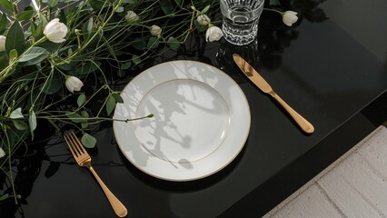Table setting with a white plate, gold cutlery, a glass of water, and green foliage. Elegant dining arrangement. Decor and tableware. Nature-inspired table setting.