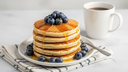 A stack of fluffy golden pancakes generously drizzled with syrup and topped with fresh blueberries, served with a mug of coffee and a fork on the side, perfect for breakfast or brunch.