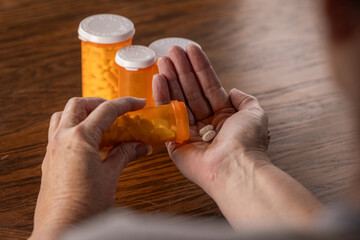 A third-person view showing the hands of a person dispensing a daily dose of pills from a bottle,...