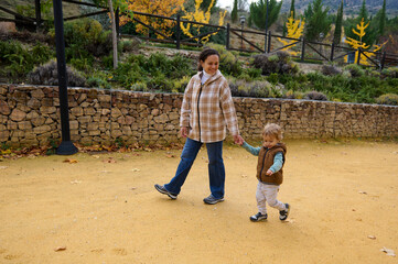 Mother Walks Hand in Hand With Her Young Child Through Autumn Park