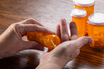 A third-person view showing the hands of a person dispensing a daily dose of pills from a bottle,...