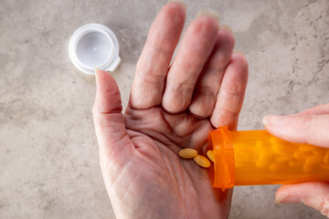A third-person view showing the hands of a person dispensing a daily dose of pills from a bottle,...