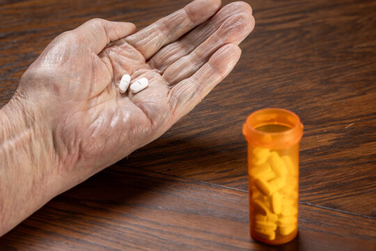 A detailed close-up shot of wrinkled, elderly senior hands carefully dosing pills from a prescription bottle. - Powered by Adobe