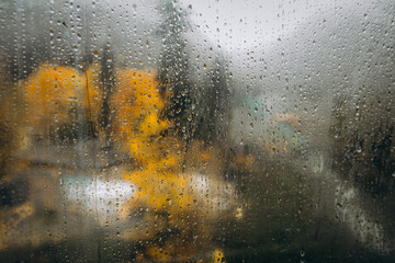 Raindrops distort a view of golden autumn trees and a misty mountain. A moody, atmospheric shot captured through a wet window, perfect for weather concepts