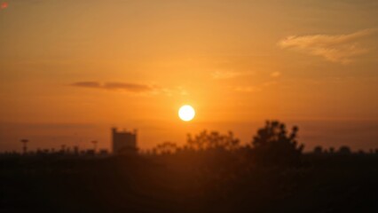 Sunset with the sun low on the horizon, silhouettes of trees, and a distant building against an orange sky.