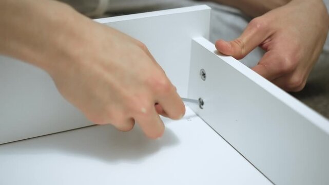 Assembler tightening corner screw with hand screwdriver while forming drawer box for dresser. Furniture maker joining inner panels using manual tool during DIY cabinet assembly. Home carpenter
