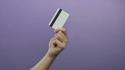 Hand of a caucasian man holding a blank credit card with a purple wall background, showcasing isolation and simplicity.