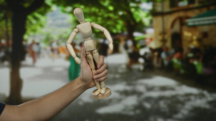 Man holding wooden mannequin on bustling city street, blending art and people, showcasing a unique outdoor perspective.