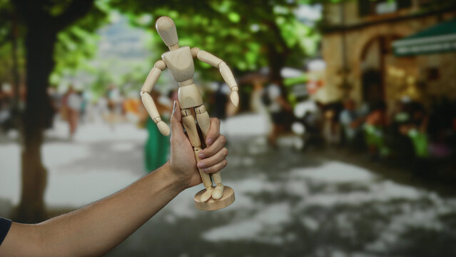 Man holding wooden mannequin on bustling city street, blending art and people, showcasing a unique outdoor perspective. - Powered by Adobe