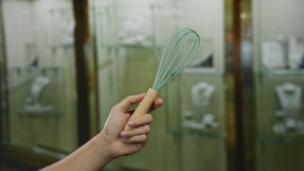 Man holding whisk in front of jewelry showcase in store captures unique indoor juxtaposition.