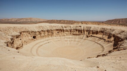 A large desert crater with concentric layers and rugged cliffs in a dry, arid landscape.