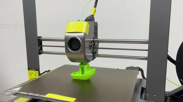 The 3D printer is printing a bright neon green Benchy boat. Ideal for modern manufacturing, prototyping, and personal technology concepts.