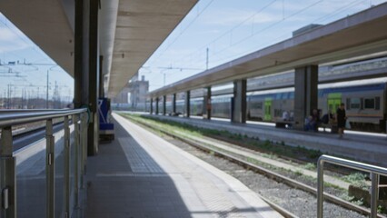 Naklejka premium Train station scene on a platform in shallow blurred focus with soft bokeh and distant trains and tracks visible; background backplate copyspace calm.