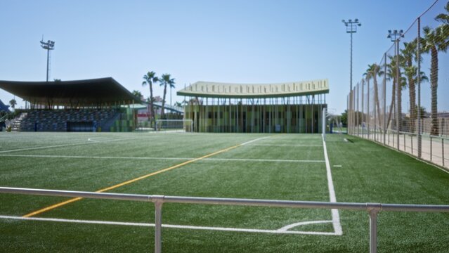 Soccer pitch and bleachers in soft blurred bokeh with shallow defocus, goalposts and palm trees hinted in distance, park; background copyspace backplate.