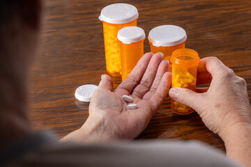 A third-person view showing the hands of a person dispensing a daily dose of pills from a bottle,...