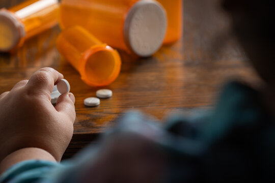 A powerful conceptual photograph showing a child's hand reaching for colorful, unattended prescription pills or medication. - Powered by Adobe