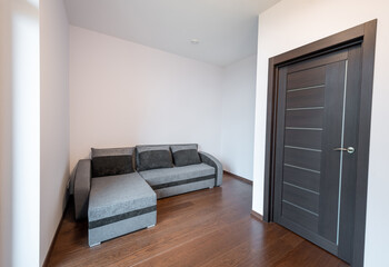 Modern sectional sofa in a minimalist room with hardwood floors and a dark interior door. Simple and elegant interior design. Home Interior