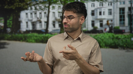 Man pinches nose on urban street with white building facade behind him expressing discomfort;...