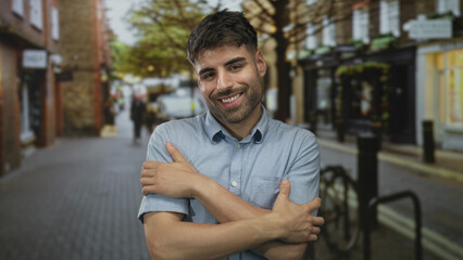 Obraz premium Man in blue short sleeve shirt holds shoulders with clasped hands smiling on urban street corner; comfort.